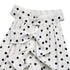 Close-up of the ruffled front detail on a white polka dot dress, highlighting the bow ties and lightweight fabric.