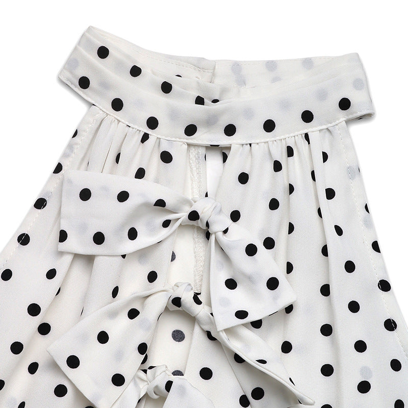Close-up of the ruffled front detail on a white polka dot dress, highlighting the bow ties and lightweight fabric.