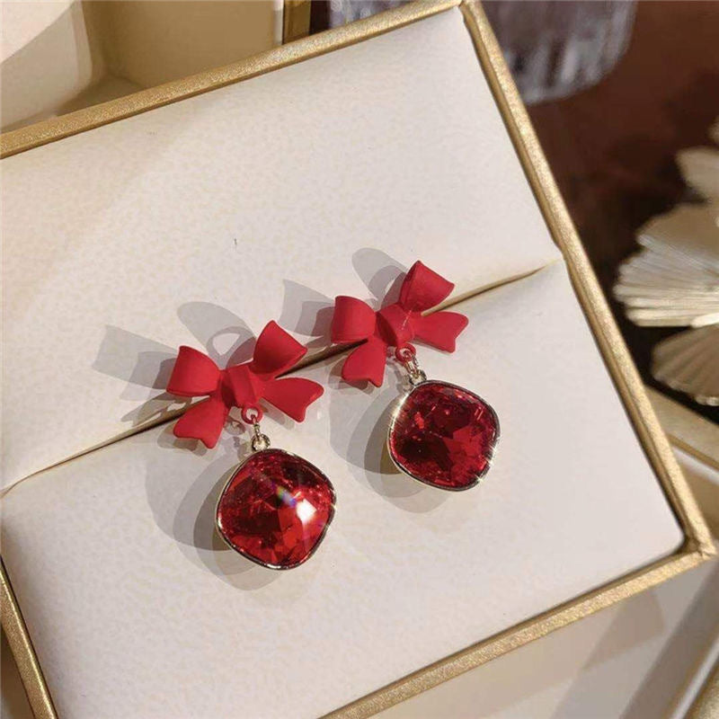 Red bow crystal earrings displayed in a gold-trimmed white jewelry box, casting shadows