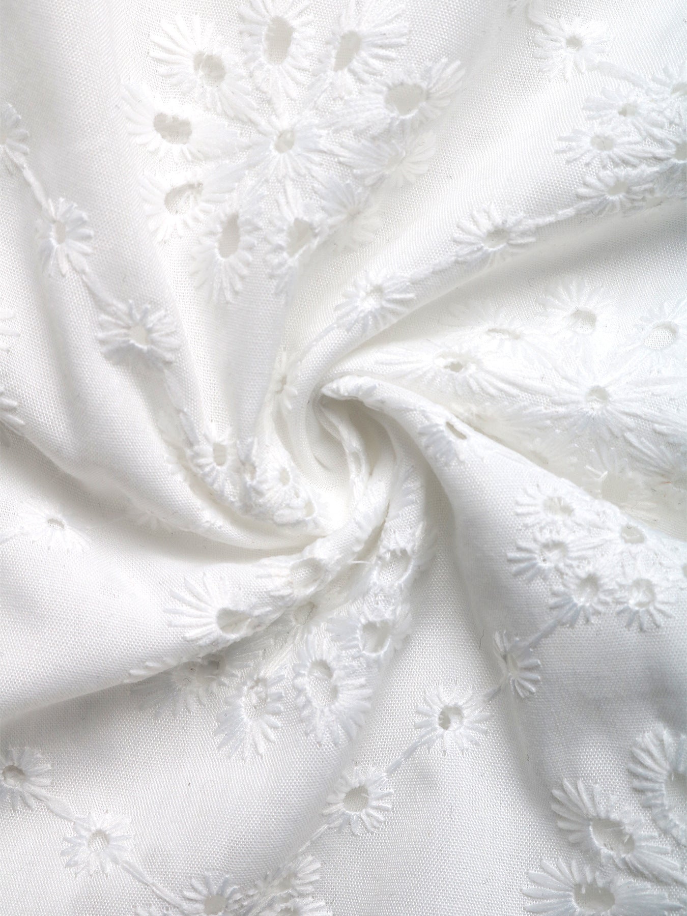 Detailed fabric shot of white floral embroidery on soft, lightweight fabric, showcasing texture and intricate cutout design.