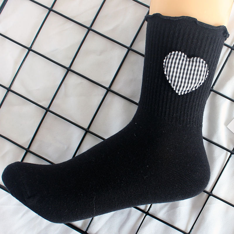 Black crew sock with gingham heart patch displayed on grid, showing ribbed texture