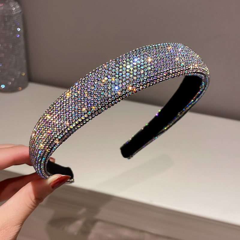 Iridescent rhinestone headband with a wide band, reflecting rainbow-colored sparkles, held by a hand with manicured nails.