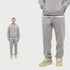 Man in light gray sweatsuit with hoodie and joggers. Close-up shows elastic waistband and white sneakers against white background