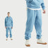 Male model wearing a light blue sweatsuit with hoodie, white undershirt layering, and matching joggers, styled with white high-top sneakers with gum soles