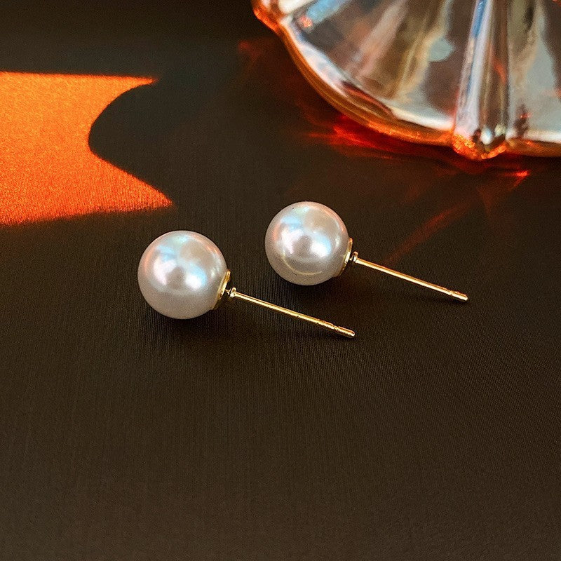 Elegant pearl stud earrings with gold posts on dark background with warm lighting and glass decor