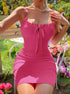 A woman wearing pink ribbed bodycon dress with tie detail sits outdoors surrounded by pink and purple garden flowers