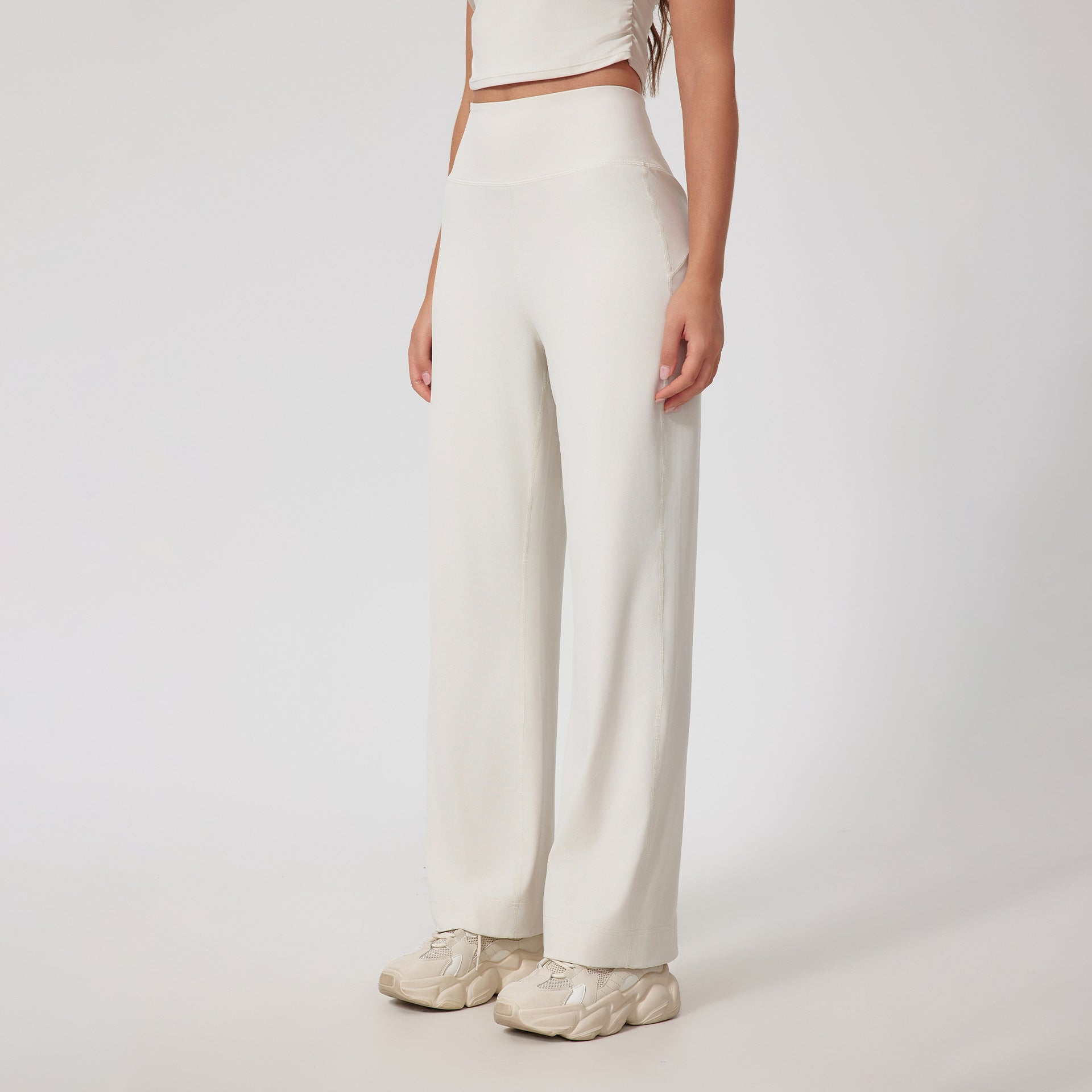 A woman wearing cream high-waisted wide-leg pants with a matching crop top and cream chunky sneakers, posing against a white background