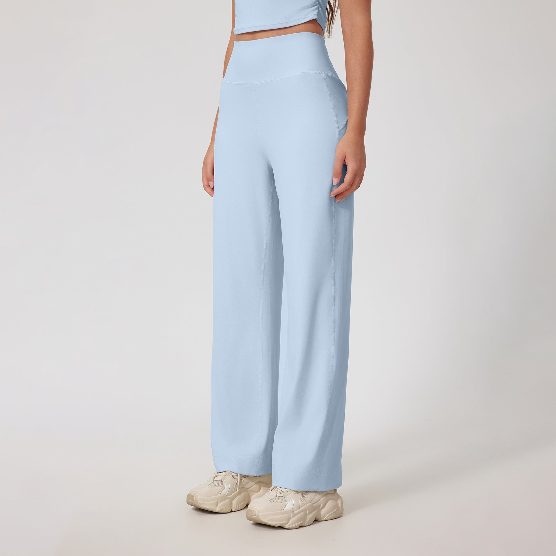 A woman wearing light blue high-waisted wide-leg pants with a matching crop top and cream chunky sneakers, standing against a white background