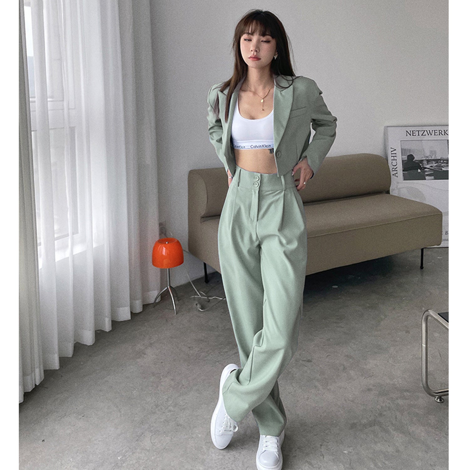 Woman in mint green suit set with white sports bra and sneakers in minimal room setting