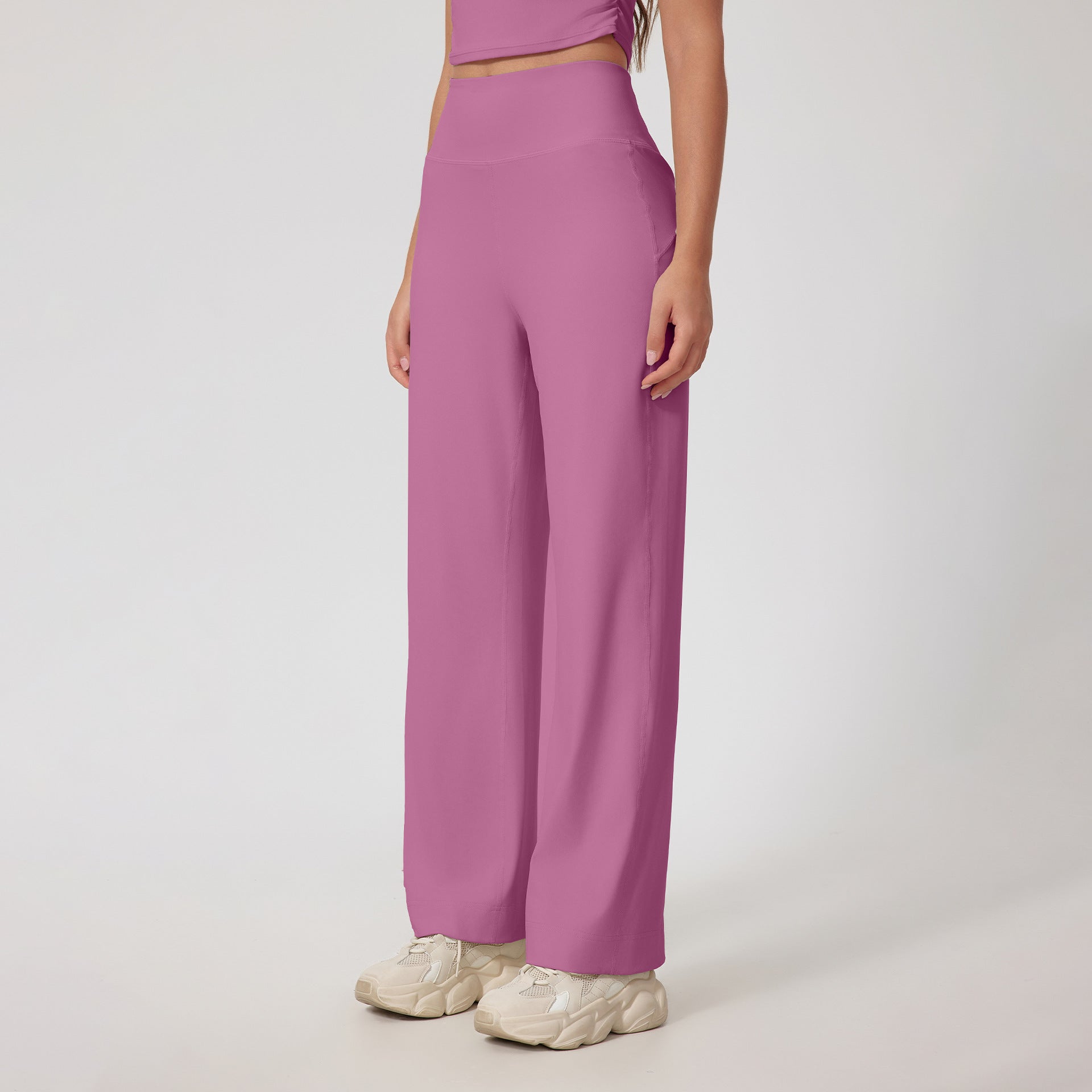 A woman wearing mauve high-waisted wide-leg pants with a matching crop top and cream chunky sneakers, posing against a white background.