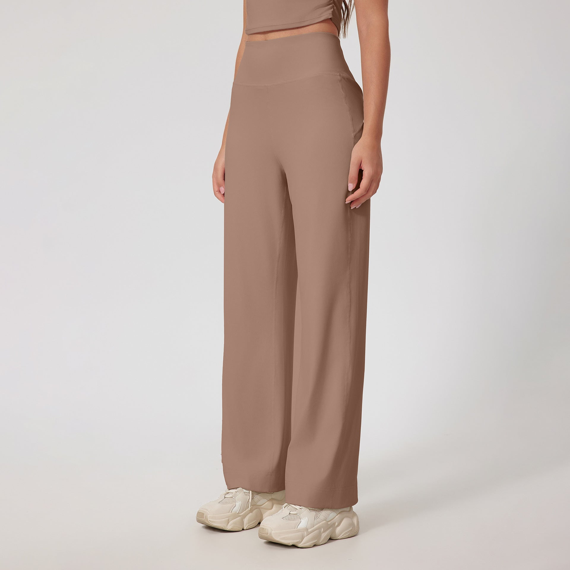 A woman wearing taupe high-waisted wide-leg pants with a matching crop top and cream chunky sneakers, standing against a white background