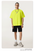 Model in neon yellow oversized t-shirt paired with black shorts, white socks and gray sneakers, featuring silver chain necklace with pendant