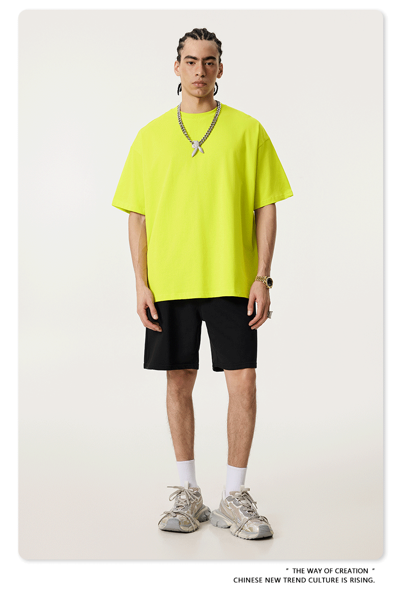 Model in neon yellow oversized t-shirt paired with black shorts, white socks and gray sneakers, featuring silver chain necklace with pendant