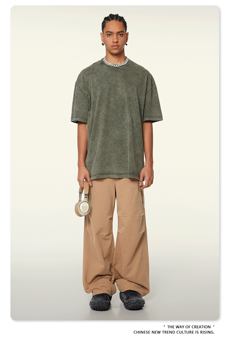 Model in olive green oversized t-shirt paired with beige cargo pants and textured footwear, wearing silver chain necklace