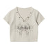 Product photo of beige crop top with V-neck metal grommets and abstract black graphic design