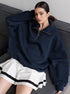 Woman wearing navy oversized quarter-zip sweatshirt with white pleated tennis skirt featuring black stripes