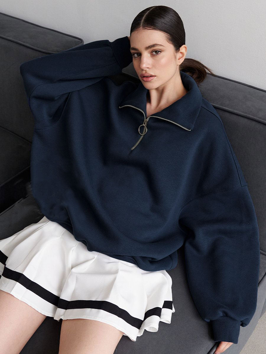 Woman wearing navy oversized quarter-zip sweatshirt with white pleated tennis skirt featuring black stripes