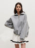 Woman in grey oversized quarter-zip sweatshirt paired with white striped-hem tennis skirt against white backdrop