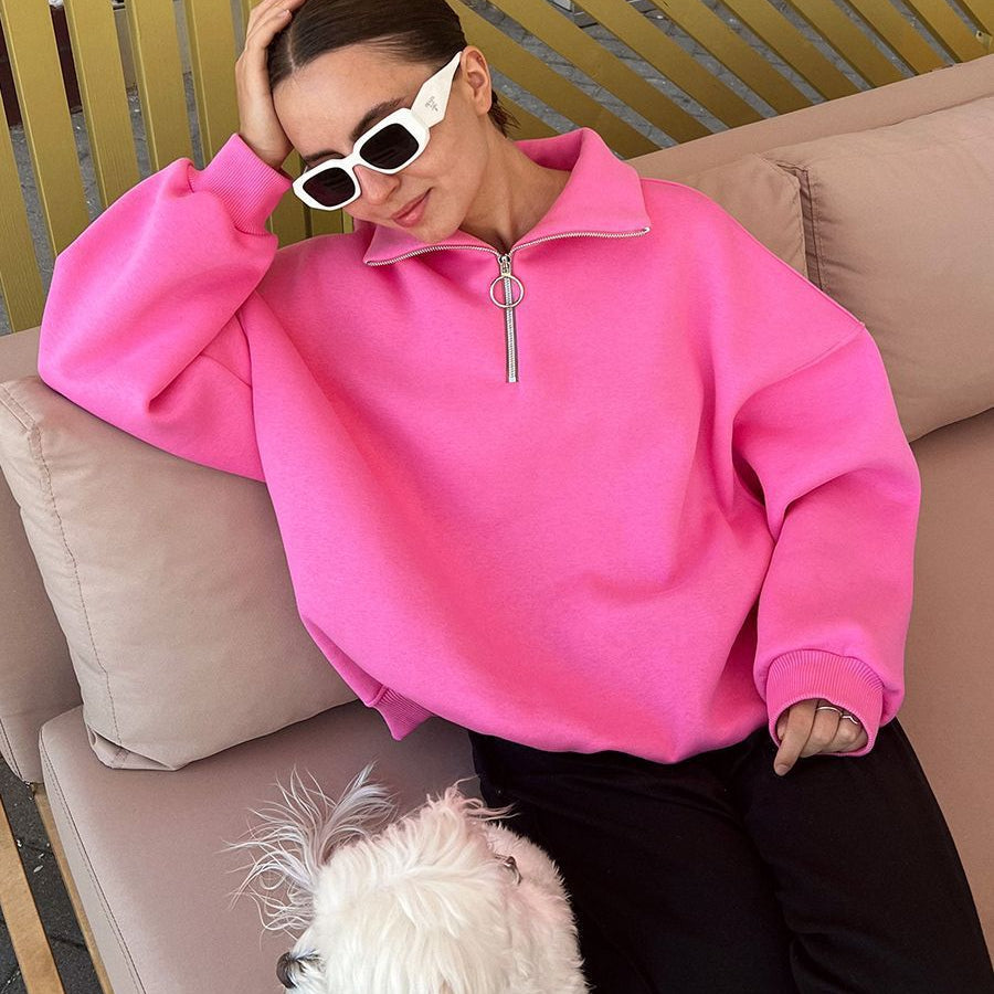 Woman relaxing on beige couch with white dog, wearing pink quarter-zip sweatshirt and white rectangular sunglasses