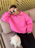 Woman relaxing on beige couch with white dog, wearing pink quarter-zip sweatshirt and white rectangular sunglasses