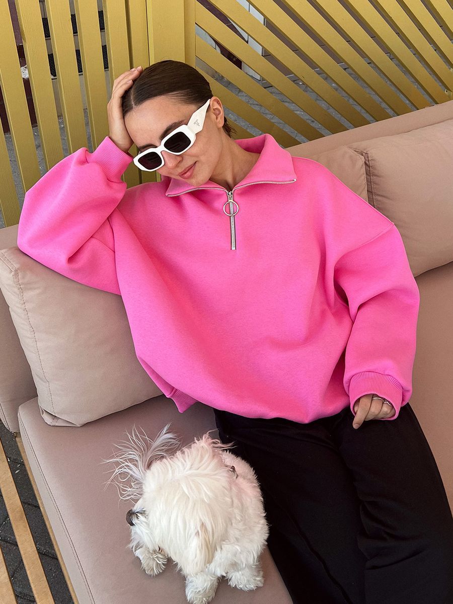 Woman relaxing on beige couch with white dog, wearing pink quarter-zip sweatshirt and white rectangular sunglasses