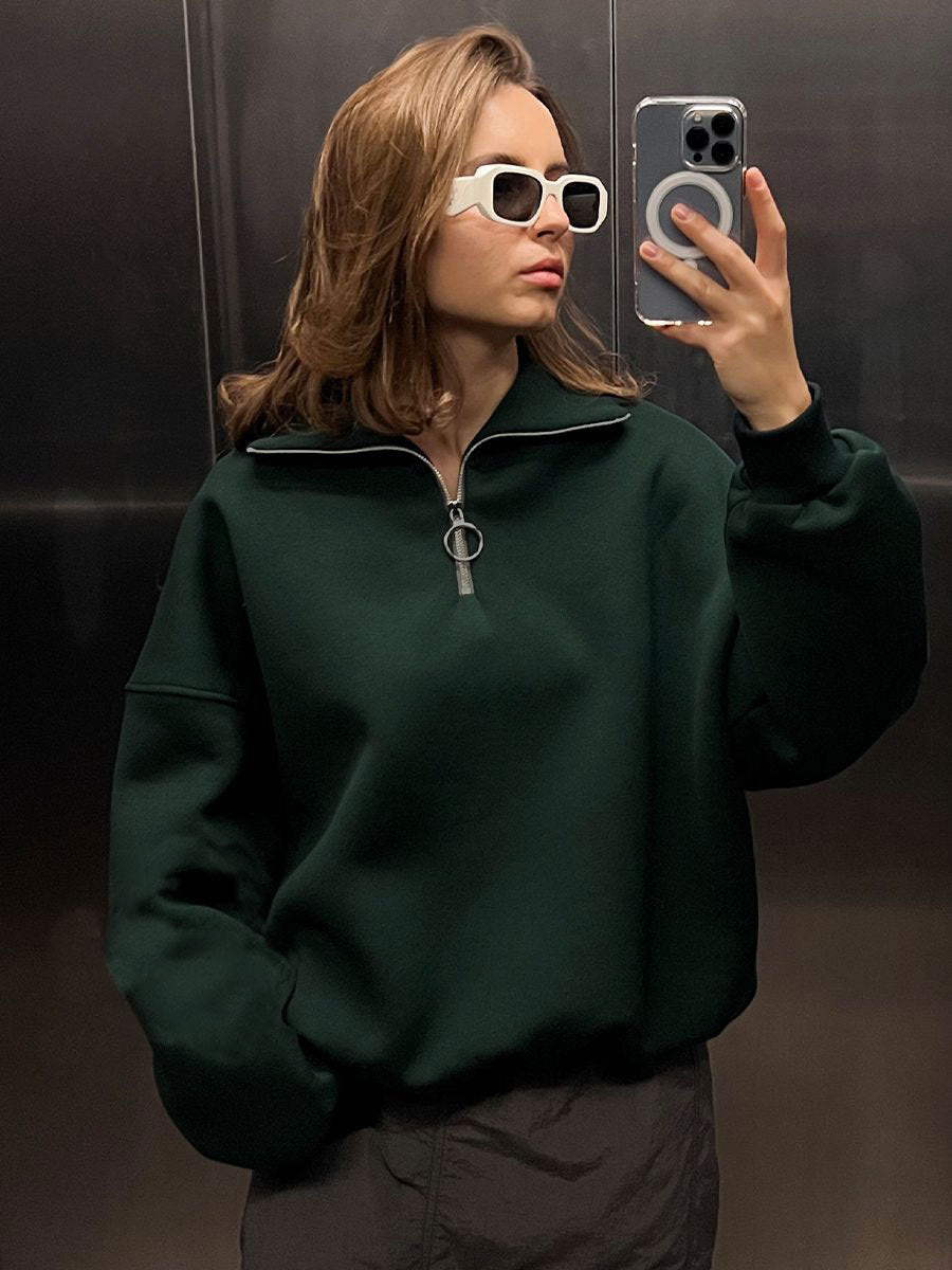 Mirror selfie of woman in forest green quarter-zip sweatshirt and white sunglasses in elevator
