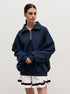 Woman in navy quarter-zip sweatshirt and white pleated tennis skirt with black stripe detail