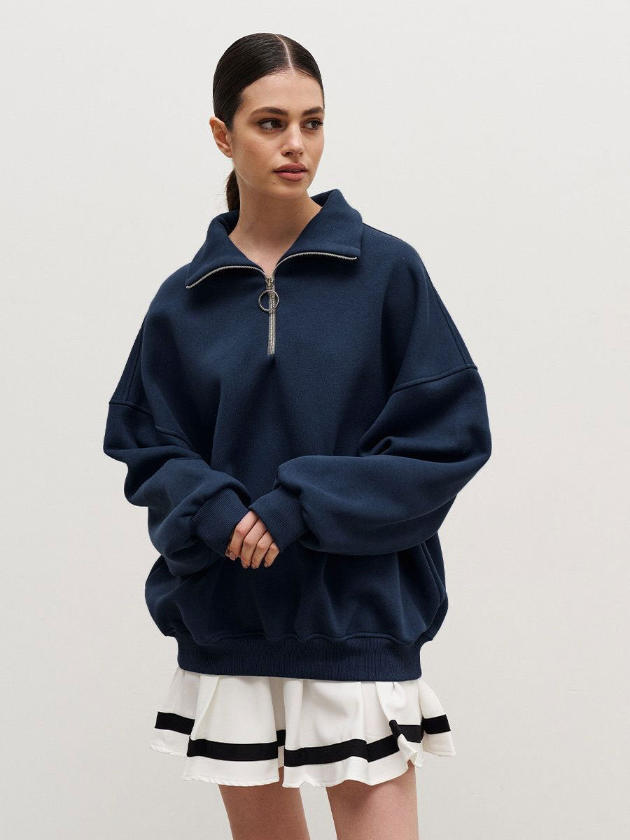 Woman in navy quarter-zip sweatshirt and white pleated tennis skirt with black stripe detail