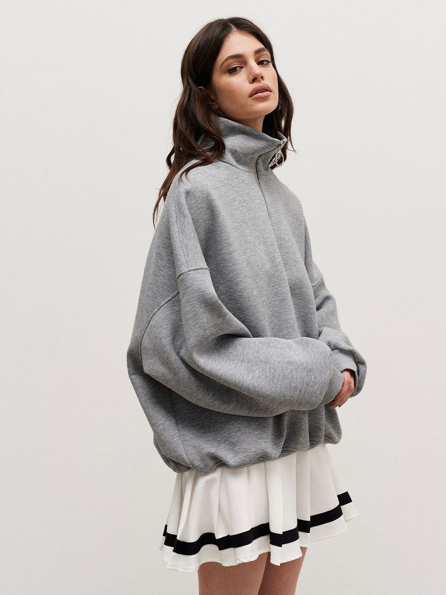 Woman wearing grey quarter-zip sweatshirt with white pleated tennis skirt and black stripe detailing