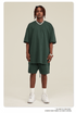 A man with short locs wearing a light sage green oversized t-shirt and matching shorts set, styled with white socks, air force ones, and a silver chain