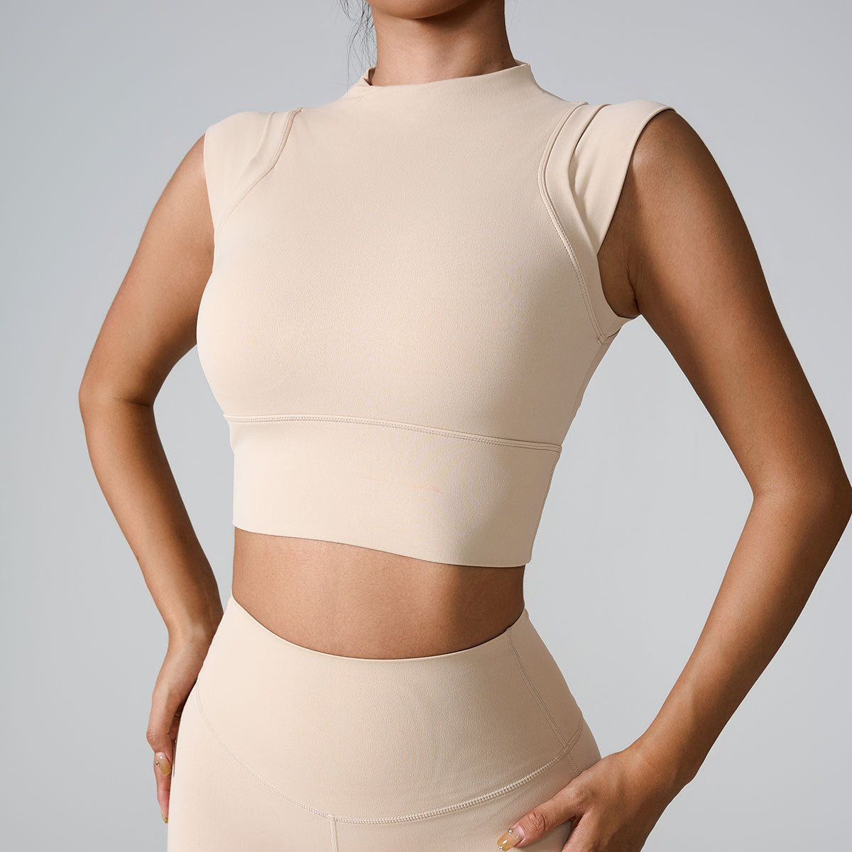 A woman is wearing a cream seamless mock neck crop top with minimalist seam details, paired with matching high-waisted leggings
