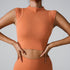 A woman is wearing a terracotta seamless athletic crop top with hands on waist, showcasing the fitted silhouette against gray background