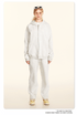 Blonde model wearing white oversized zip-up hoodie and matching sweatpants with white sunglasses on head and yellow shoes against cream background
