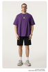 Model wearing purple oversized t-shirt with black shorts and chunky gray sneakers, accessorized with silver chain necklace featuring white pendant