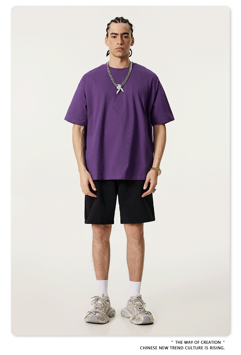 Model wearing purple oversized t-shirt with black shorts and chunky gray sneakers, accessorized with silver chain necklace featuring white pendant
