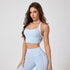 A woman is posing with hand on thigh wearing a light blue sports bra with white trim and coordinating leggings with dual white stripes