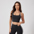 A woman is standing with hand resting on waist in a black racerback sports bra with white trim and matching striped leggings