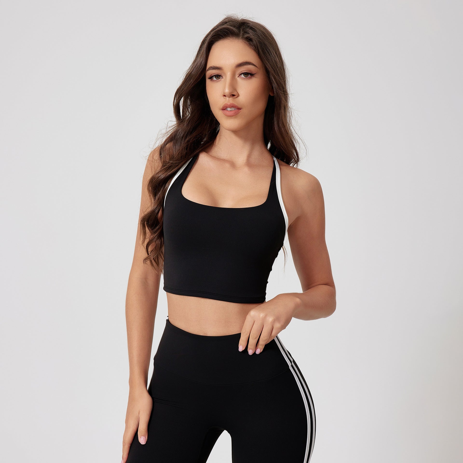 A woman is posing with one hand down wearing a black sports bra with white trim detail and high-waisted leggings with side stripes