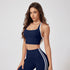 A woman is standing in a navy blue racerback sports bra with white trim and matching high-waisted leggings with double white stripes