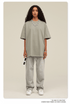 Woman wearing light sage green oversized t-shirt with light gray sweatpants, white sneakers and beaded necklace, holding white sunglasses