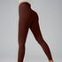 Model in brown high-waisted leggings and cream top, side view showing seamless construction on gray backdrop