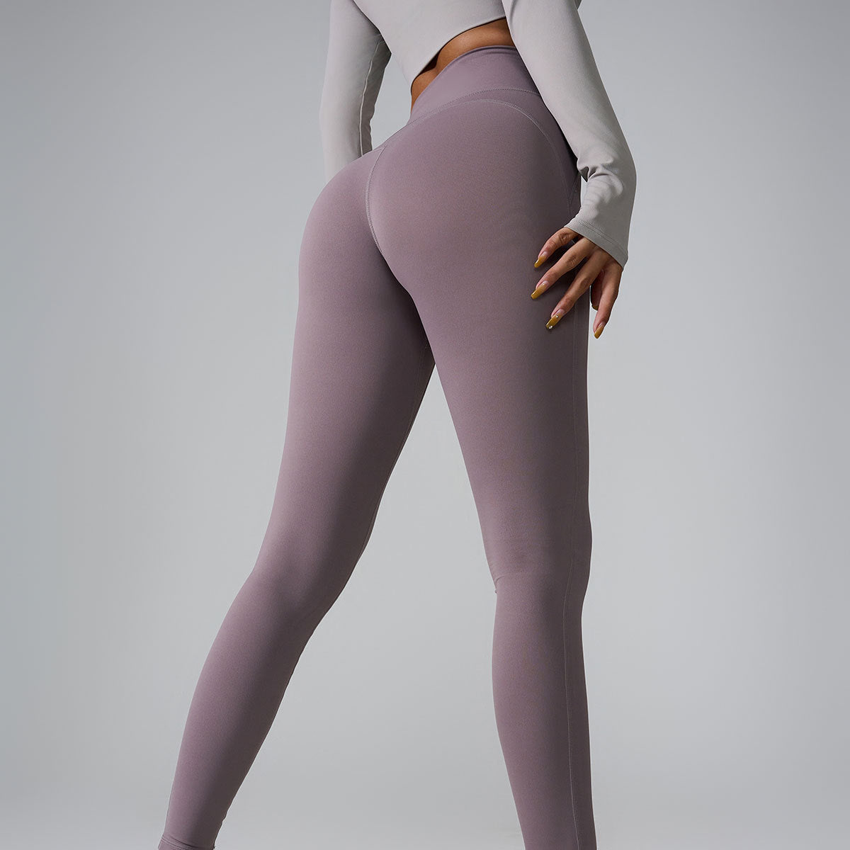 Model wearing fitted gray long-sleeve sweatshirt, mauve high-waisted leggings, and white sneakers in studio setting