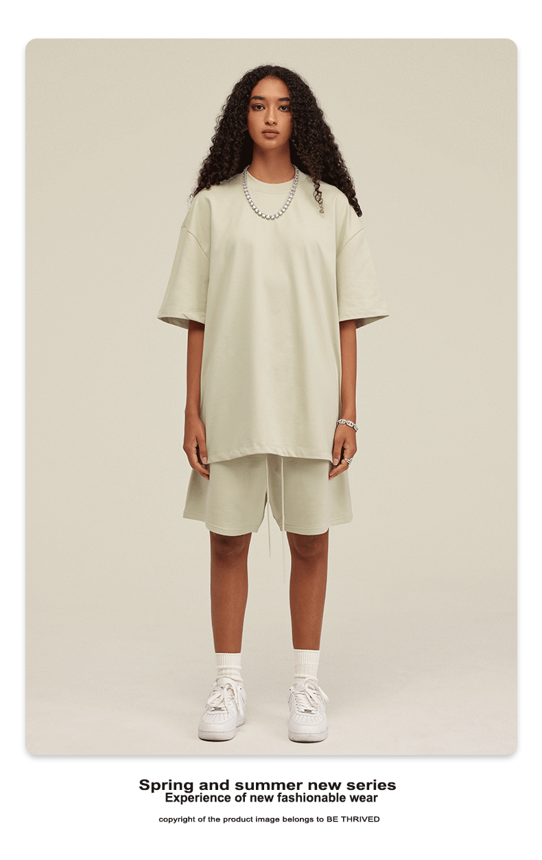 Model with curly hair wearing oversized cream t-shirt and matching shorts with white socks and white sneakers against cream background