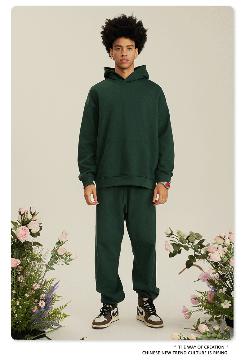 Man with curly hair wearing forest green hoodie and matching pants with brown and white sneakers