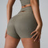 A model in olive green ribbed workout shorts with waist cutouts and matching sports bra, side angle, studio setting