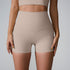 A model wearing beige high-waisted ribbed compression shorts and matching sports bra, photographed against light gray backdrop
