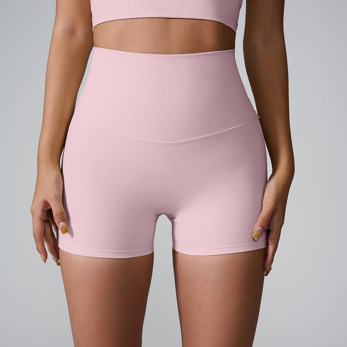A model wearing pink ribbed high-waisted compression shorts and matching sports bra, front view against gray background