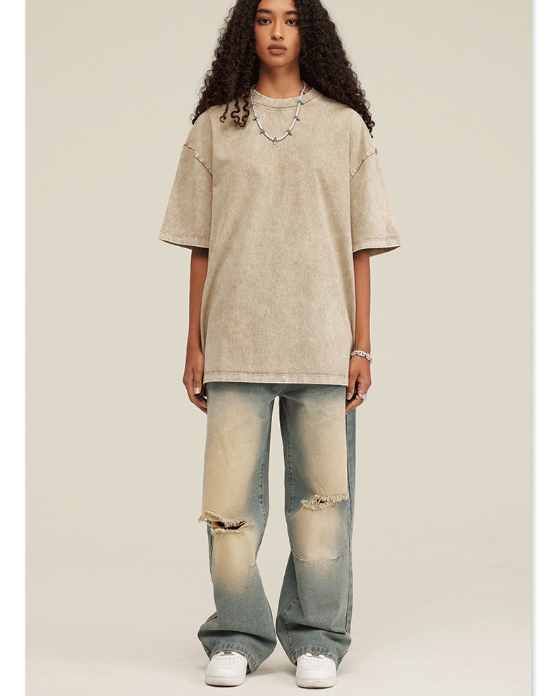 Woman wearing oversized beige acid-washed t-shirt with light wash distressed jeans and white sneakers against neutral background