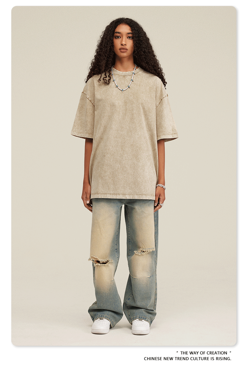 Woman wearing oversized beige acid-washed t-shirt with light wash distressed jeans and white sneakers against neutral background