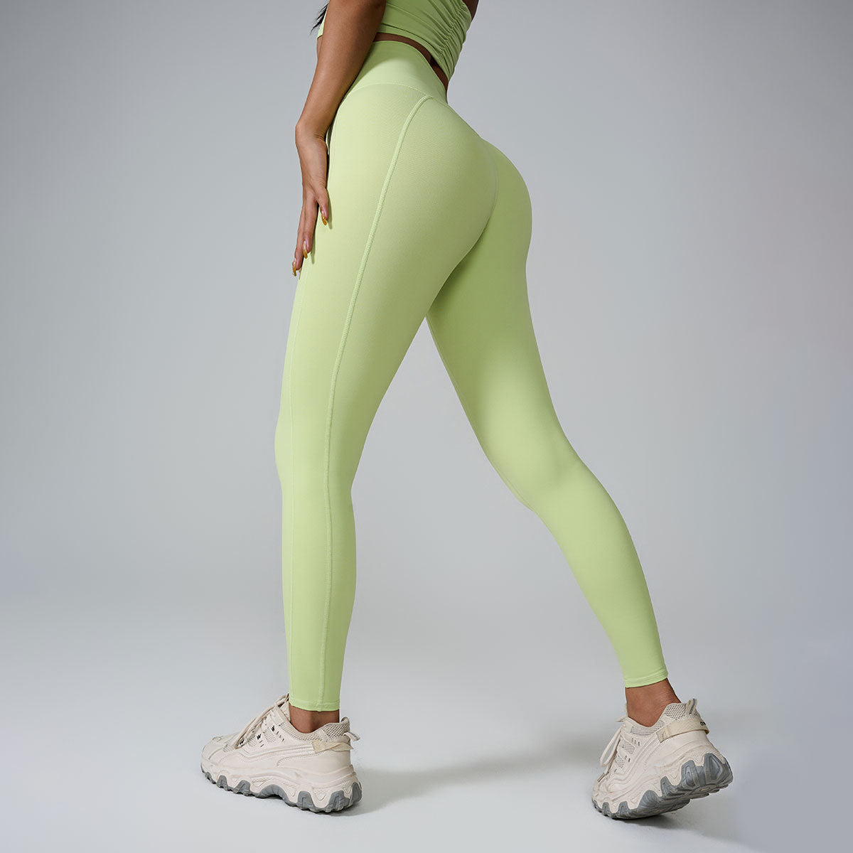 A model wearing light green workout leggings and matching top, showing back view with chunky white sneakers